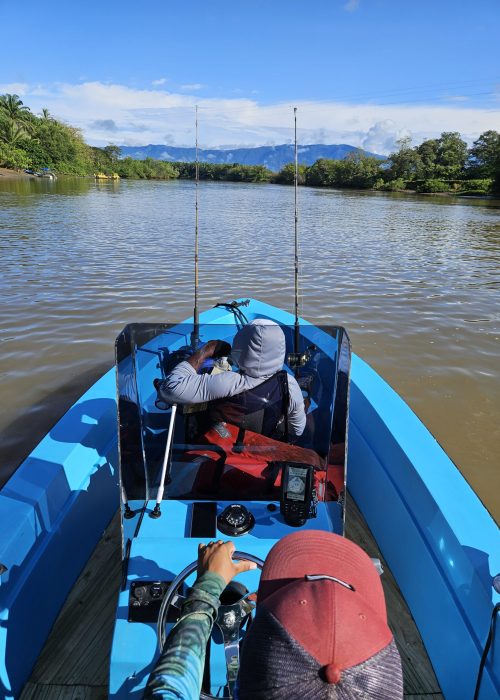 blue fishing boat on the water with two people fishing